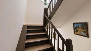 Una escalera de madera con barandillas oscuras, una ventana pequeña con una planta y un cuadro en la pared.