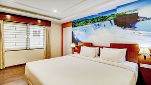 Habitación de hotel con una cama grande, una ventana con persianas, un mural en la pared de una cascada y una mesita de noche con una lámpara.