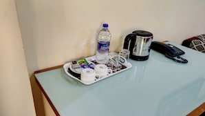 Una mesa con una botella de agua, cafetera, teléfono y varios vasos y sobres.