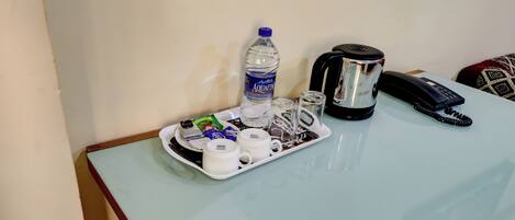 A table with a water bottle, coffee maker, phone, and various cups and packets.