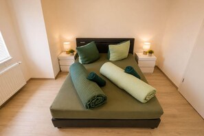 Una cama bien hecha con almohadas y toallas dobladas, dos mesitas de noche con lámparas y un radiador en la pared.