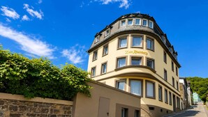 A building with a curved facade, a stone wall with 'Zum Rheinberg' signage, and a clear blue sky. - Zum Rheinberg – Marksburg Panorama (Braubach)
