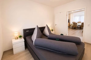 A modern bedroom with a bed, bedside tables, and a view into the dining area.
