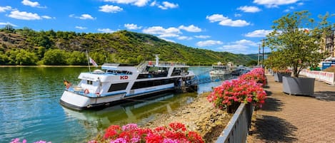 A riverboat docked at a pier with a clear sky and lush greenery in the background.