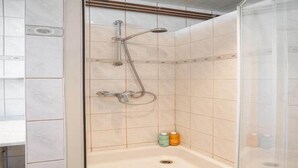 Lasiseinällä varustettu suihku, käsisuihkupää ja kaksi shampoopulloa lattialla.
