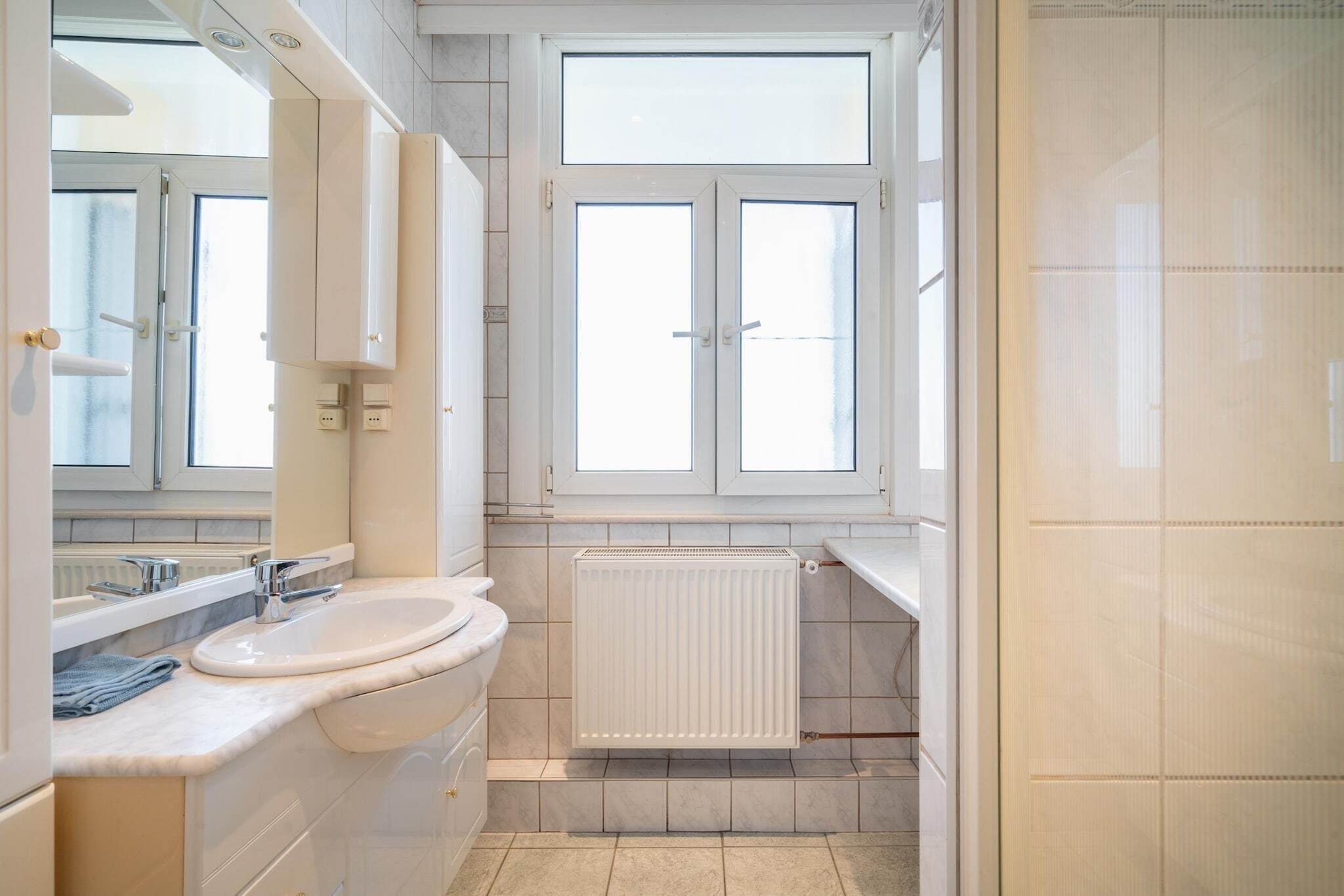 A bathroom with a double sink, a mirror, a window, and a radiator.