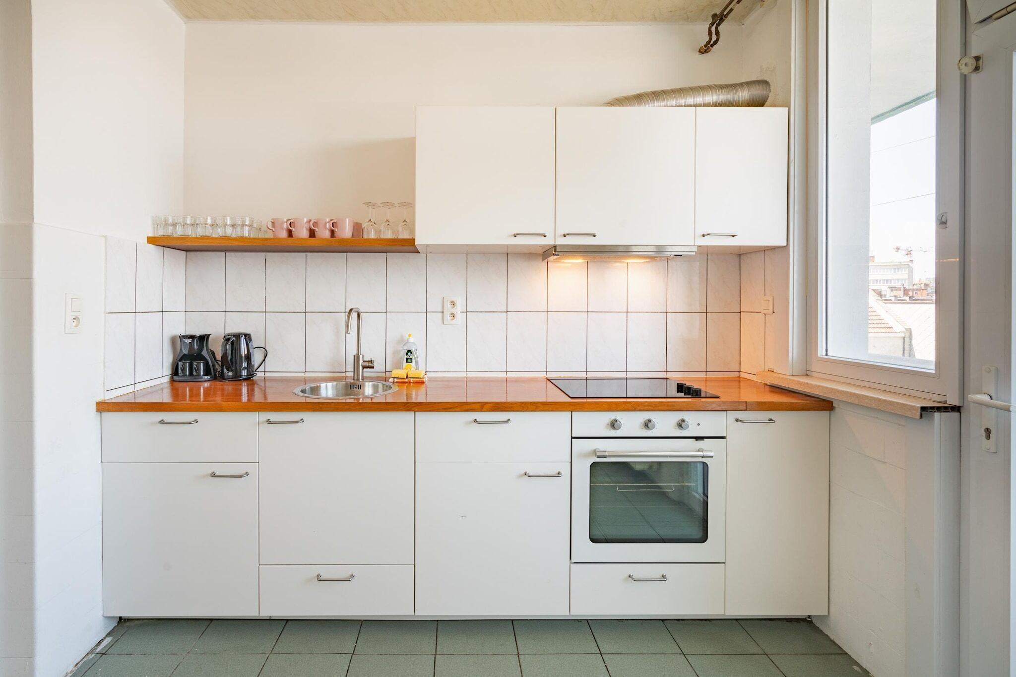 A kitchen with white cabinets, a stainless steel sink, a stove, and a window.