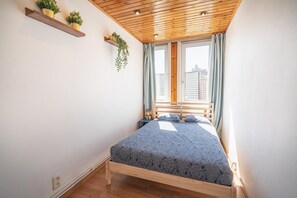 A bedroom with a wooden ceiling, a bed with a patterned bedspread, a window with curtains, and two wall-mounted shelves with plants. - Family-Friendly 3-Bedroom Apartment for 6 Guests (Antwerp)
