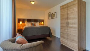 A hotel room with a bed, bedside lamps, a wardrobe, and a chair.