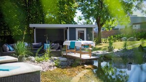 A serene outdoor setting with a small pond, a wooden deck, and a relaxation area with a massage table.
