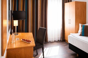 Ein Hotelzimmer mit einem Bett, einem Schreibtisch mit Lampe, einem Stuhl und einer Schale Erdbeeren.