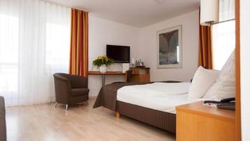 Una habitación de hotel con cama, escritorio, silla, televisor y ventana con cortinas.