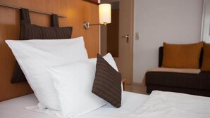 Et hotelværelse med en pænt redt seng, en sengebordlampe og en sofa med puder.