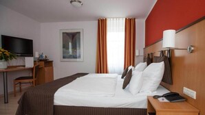 Una camera d'albergo con un letto, una scrivania, una televisione e una finestra con tende.
