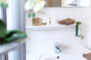 Et badeværelse med en hvid vask, et spejl og en hylde med håndklæder og toiletartikler.