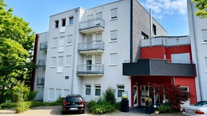 A multi-story residential building with balconies, a red and grey facade, and a parking area with cars. - Stuttgart Großbettlingen Hotel by Belvilla Family Apartment (Großbettlingen)