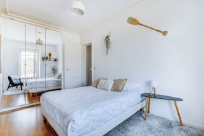 Ein Schlafzimmer mit einem Bett, einem Nachttisch, einer Lampe und einer hängenden Pflanze.