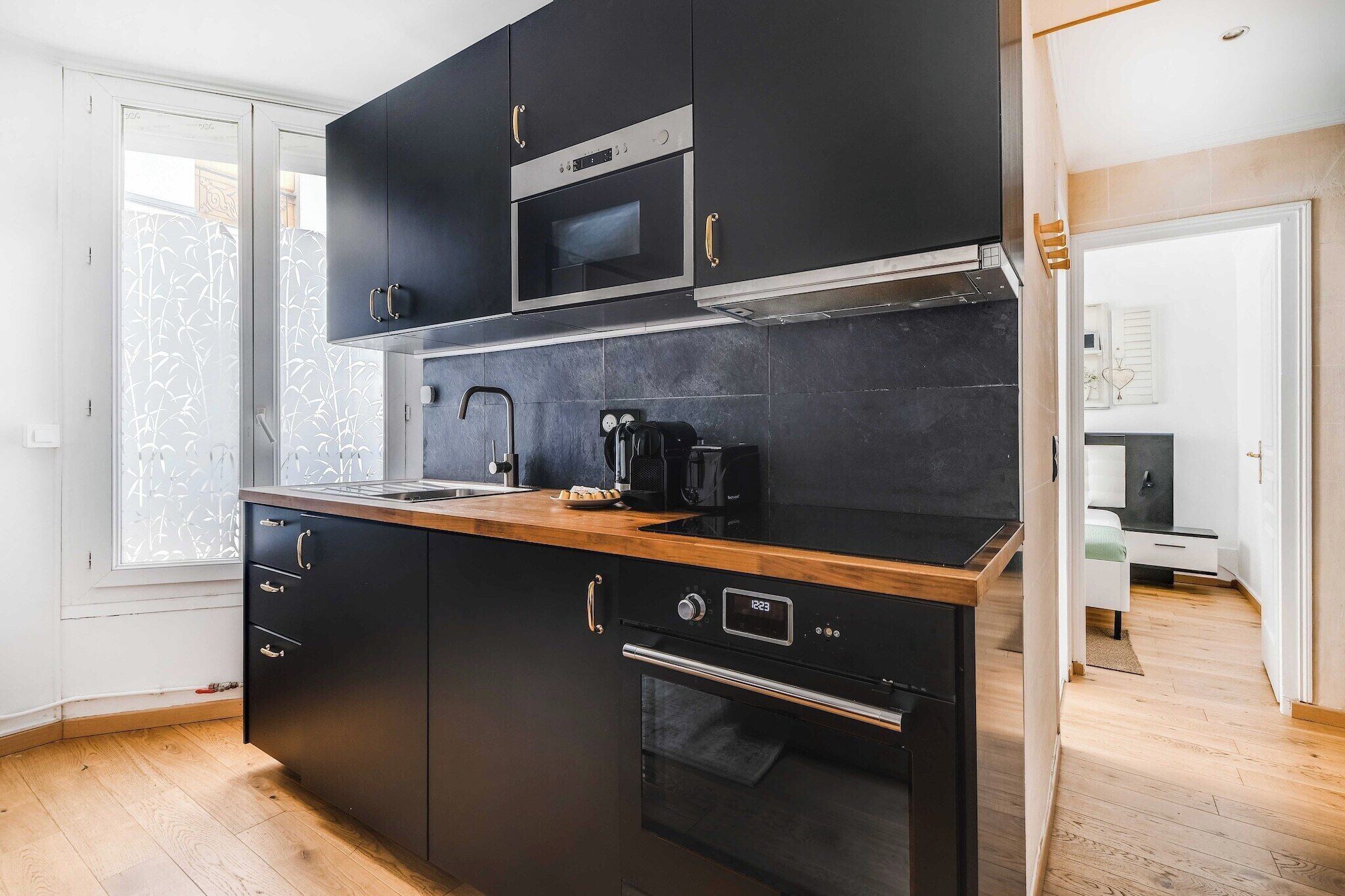 A modern kitchen with black cabinetry, a stainless steel microwave, a coffee maker, and an oven.
