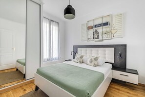 A bedroom with a bed, bedside tables, a hanging light fixture, a window with curtains, and wall decorations. - Cozy Apartment 1BR/4P - La Villette (Paris)