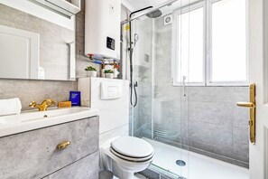 A modern bathroom with a shower, toilet, vanity, and a glass-enclosed shower area. - Cozy Apartment 1BR/4P - La Villette (Paris)