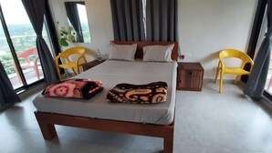 Habitación de hotel con una cama, dos sillas, una mesita de noche y ventanas amplias.