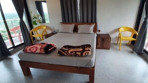 A hotel room with a large bed, two chairs, a small table, and a view of the outdoors. - Hotel Randha (Akola)