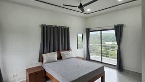 A bedroom with a bed, a nightstand, a ceiling fan, and a large window with curtains. - Hotel Randha (Akola)