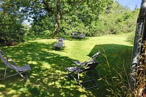 Un espace extérieur aménagé avec des chaises et une table en métal, entouré d’une végétation luxuriante et d’arbres.