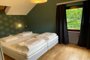 Un dormitorio con cama, mesita de noche, lámpara, ventana con cortinas y vista a zonas verdes.