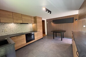Une cuisine moderne avec des meubles en bois, une cuisinière noire et un coin repas comprenant une table et des chaises.