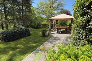 Un jardin agrémenté d’un belvédère, d’une balançoire et d’un chemin pavé.