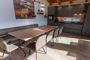 Una cocina moderna con una mesa y sillas de madera, un cuadro en la pared y lámparas colgantes.