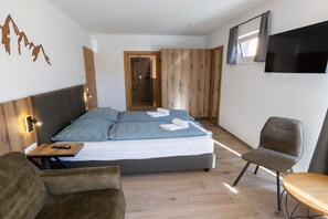 A modern bedroom with a bed, two chairs, a small table, a TV, and a shower area. - Ski-in/ski-out chalet with beautiful view (St. Lambrecht)