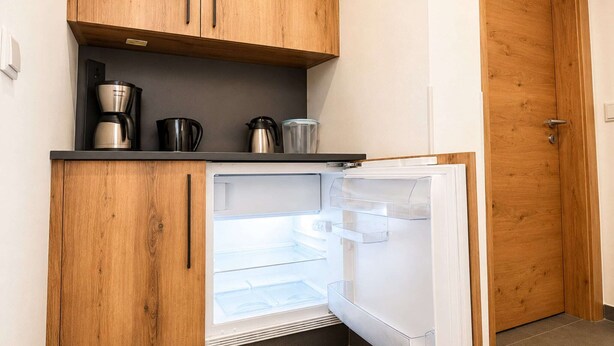 Een compacte keuken met een geïntegreerde koelkast, houten kastjes en een koffiezetapparaat op het aanrecht.