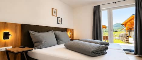 A hotel room with a large bed, wooden headboard, bedside lamps, a small table, and a view of the outdoors.