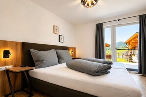 A hotel room with a large bed, wooden headboard, bedside lamps, a small table, and a view of the outdoors. - Ski-in/ski-out chalet with beautiful view (St. Lambrecht)