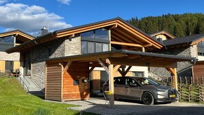 Een modern huis met twee verdiepingen, een stenen gevel, een overdekte autoverrijzing en een geparkeerde auto.
