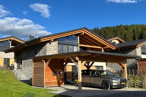 A modern two-story house with a stone facade, a covered carport, and a car parked inside. - Ski-in/ski-out chalet with beautiful view (St. Lambrecht)