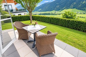 A patio with wicker furniture, a glass door, and a view of a green landscape with mountains. - Apartment in Mittersill with terrace (Mittersill)