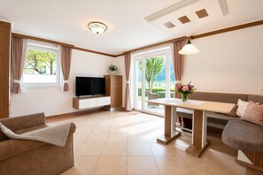 Ein modernes Wohnzimmer mit Sofa, Fernseher, Esstisch und Blick ins Grüne.