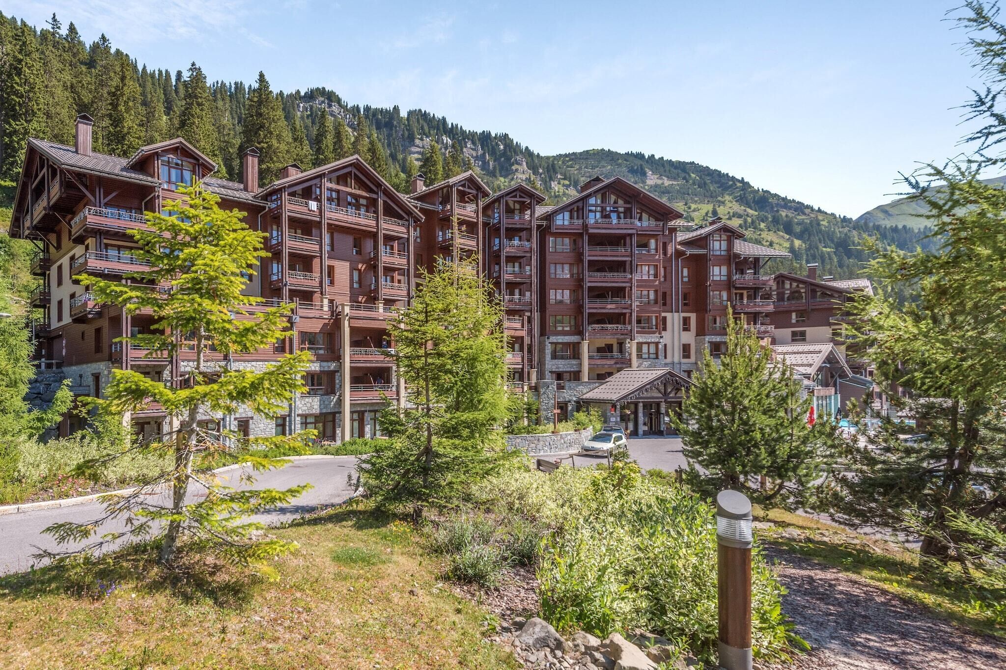 A multi-story hotel with balconies, surrounded by trees and mountains.