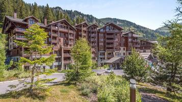 A multi-story hotel with balconies, surrounded by trees and mountains.
