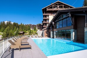 A hotel with a swimming pool, lounge chairs, and a view of other buildings. - Scenic 4-Person Mountain View Retreat (Flaine)