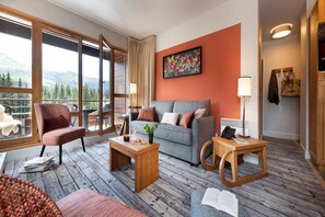 A cozy living room with a sofa, armchair, and coffee table, a large window with a mountain view, and a painting on the wall. - Mountain View Retreat with Balcony for 8 (Flaine)