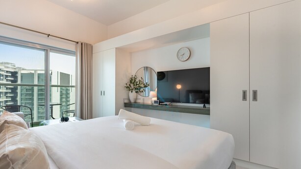 Habitación de hotel moderna con una cama grande, televisión, planta y vista a la ciudad.