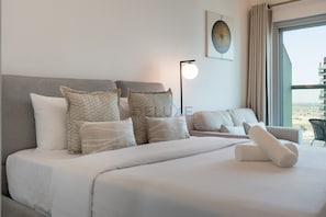 A hotel room with a large bed, multiple pillows, a bedside table, a lamp, and a window with curtains. - High-Floor Studio with Community Views, Moments from Dubai Butterfly Garden (Dubai)