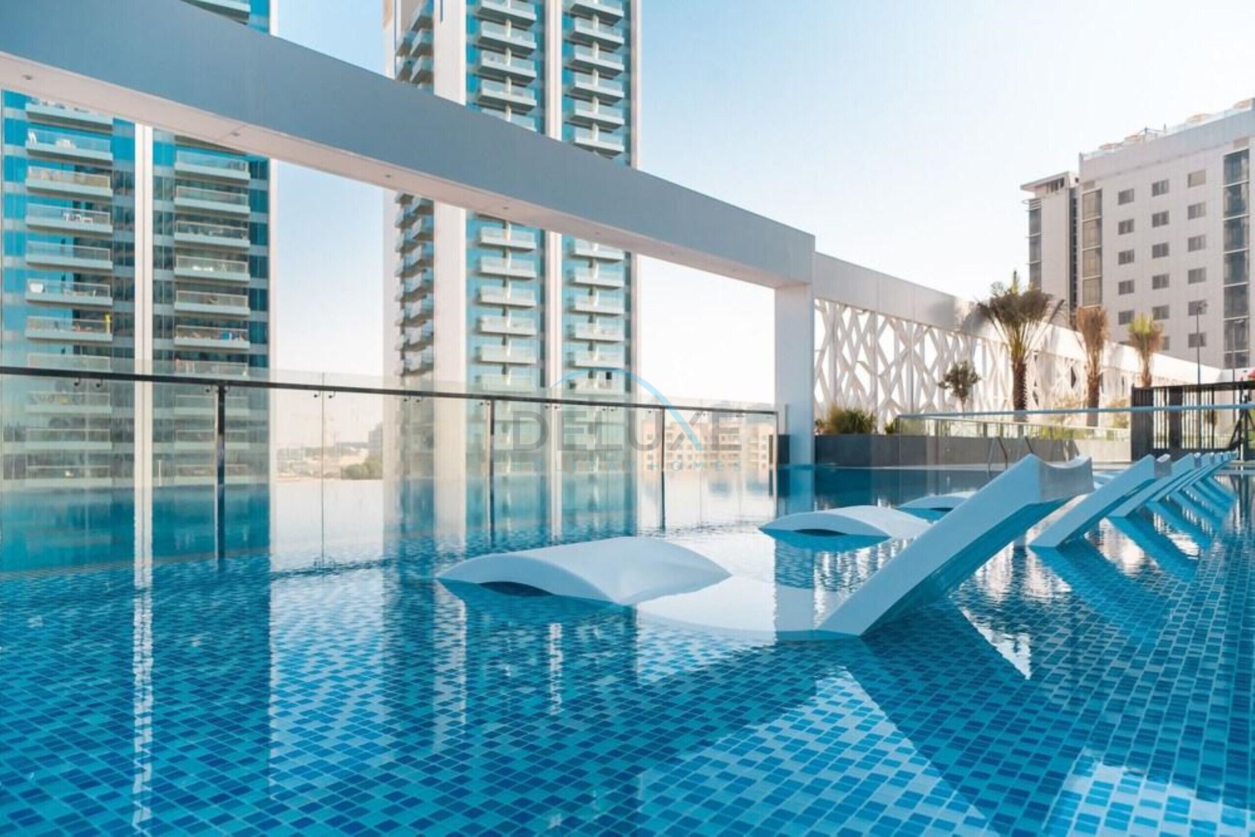 An indoor swimming pool with clear blue water, surrounded by modern buildings and a glass barrier.