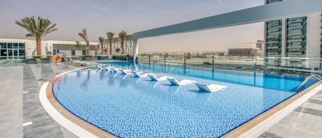 A rooftop swimming pool with clear blue water, surrounded by a modern building with large windows.