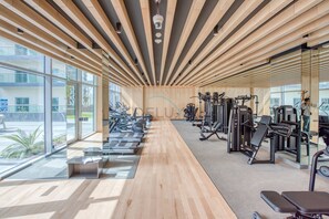 Ein Fitnessraum mit Trainingsgeräten, großen Fenstern und einer Holzbalkendecke.