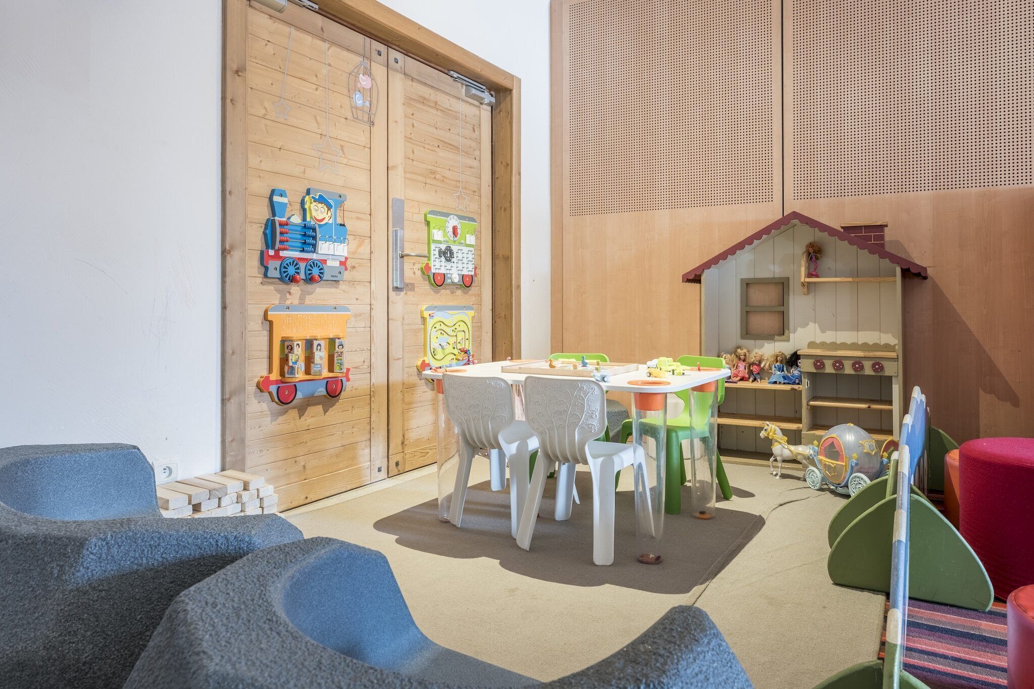 Ein Spielzimmer für Kinder mit Holztür, Tisch und Stühlen sowie verschiedenen Spielzeugen.